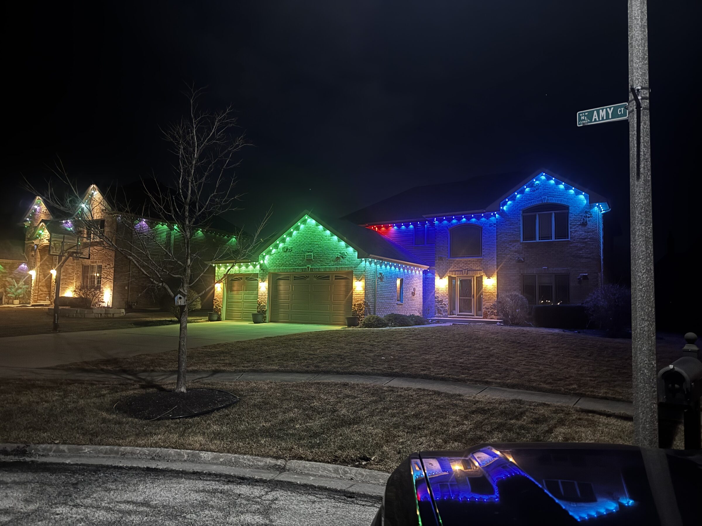 Permanent track lighting illuminating a home's roofline in color at night